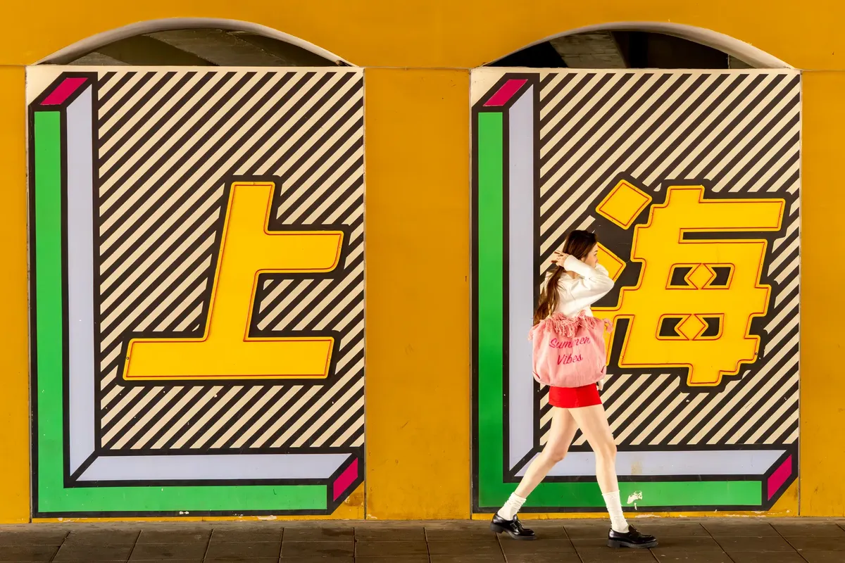 A woman walks past a colorful mural depicting Shanghai. Bright and artistic street scene.