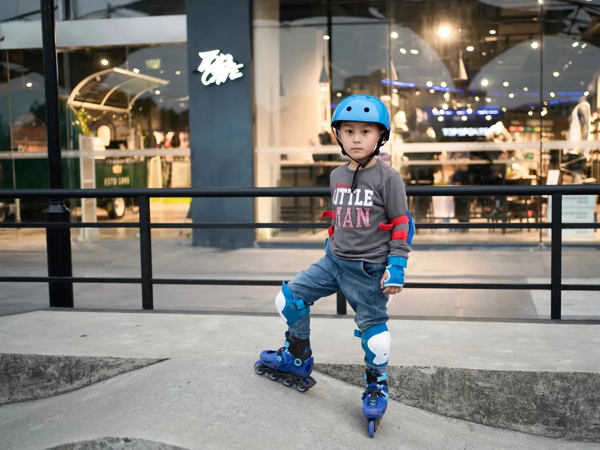 Child wears protective gear and roller skates near a shopping area in Shanghai, China.