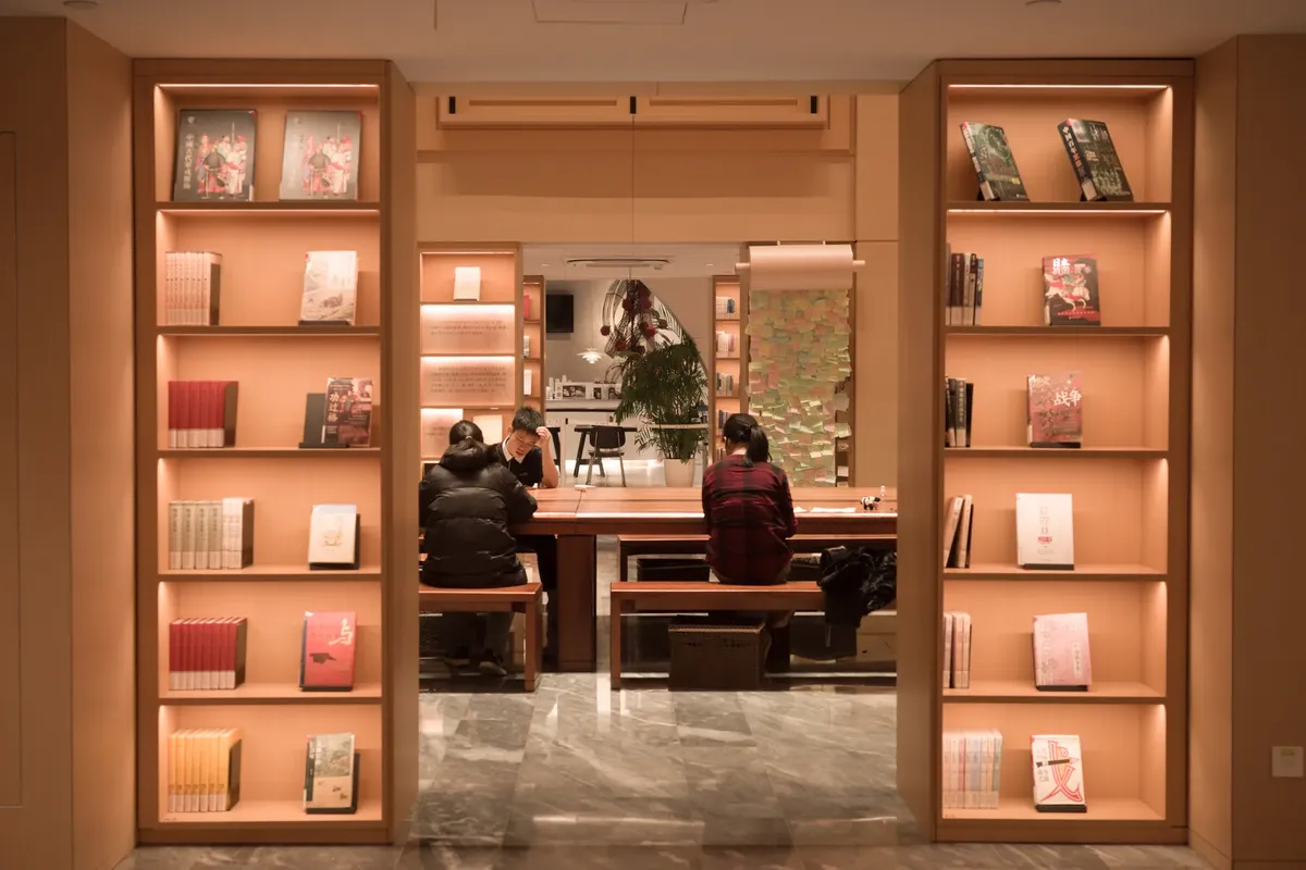 Cozy library interior in Shanghai featuring people reading at a table surrounded by illuminated bookshelves.
